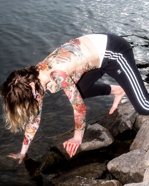 actress with colourful t-shirt crowching on rocks at water edge
